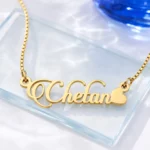 Gold-tone decorative script name necklace with a heart on a clear glass display