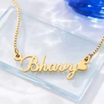 Gold-tone curved script name necklace with a heart on a clear glass display