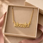 Gold-tone Indian style name necklace displayed in an open beige jewellery box