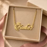 Gold-tone name necklace with crown, star and heart accents displayed in an open beige jewellery box