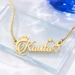 Gold-tone name necklace with crown, star and heart accents on a clear glass display