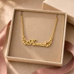 Gold-tone angel wings name necklace displayed in an open beige jewellery box