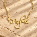 Cursive Curved Name Necklace with original gold box chain on travertine hero background
