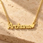 Gold Archana name pendant with solid heart and box chain on travertine stone