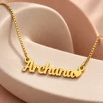 Gold Archana name pendant with solid heart and box chain on curved ceramic