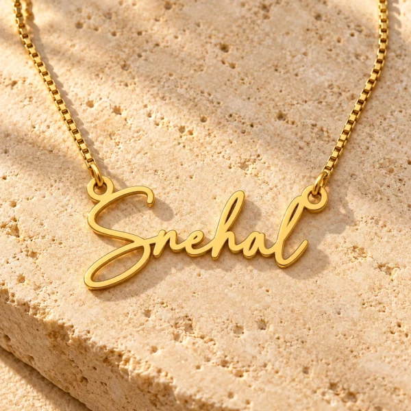 Gold Snehal signature name pendant and box chain on travertine stone
