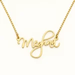Gold cursive Meghna name necklace with box chain on ivory background