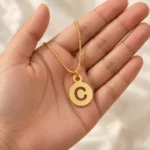 Round Letter Pendant with a chain held in a hand