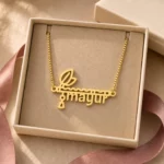 Gold-tone flute and feather name pendant displayed in an open beige jewellery box