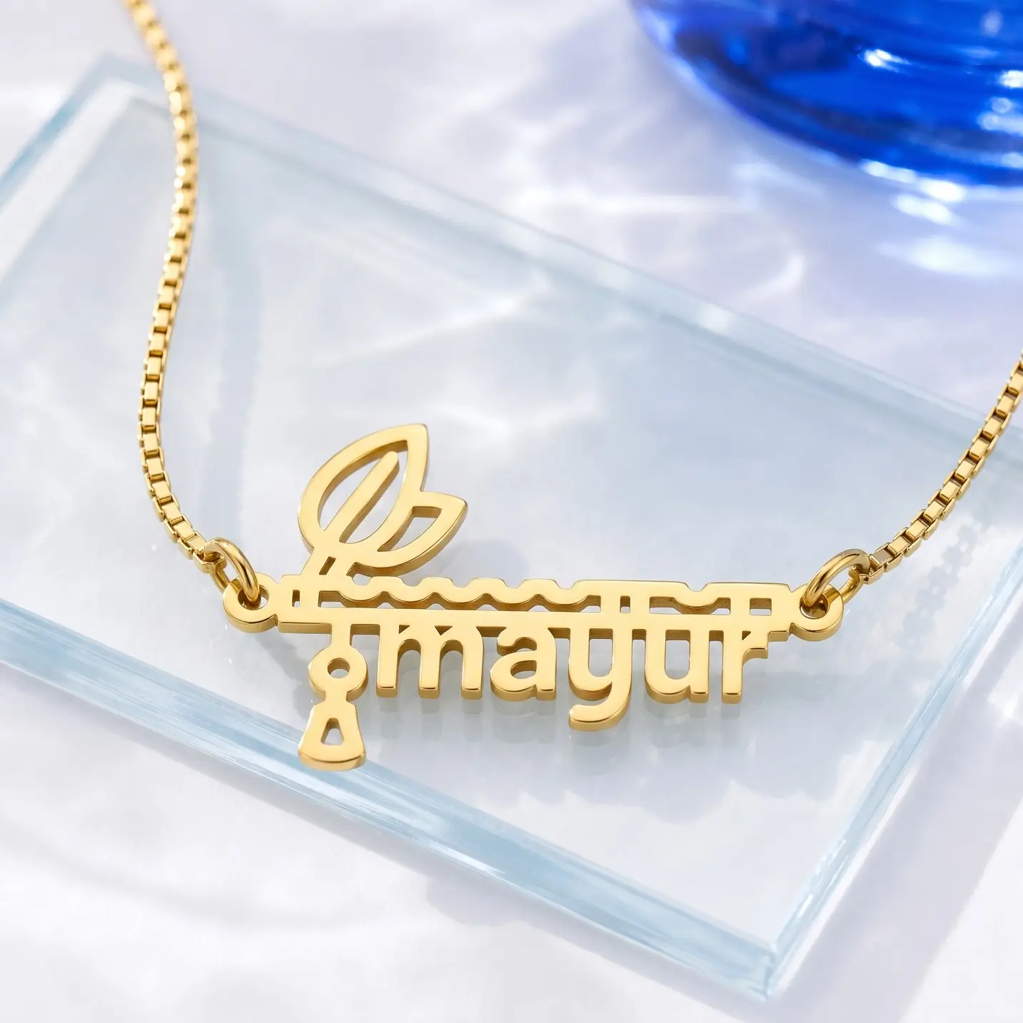 Flute and Feather Name Pendant - Glass Display Gold-tone flute and feather name pendant on a clear glass display