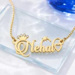 Gold-tone name necklace with a sparkling crown, star and heart on a clear glass display