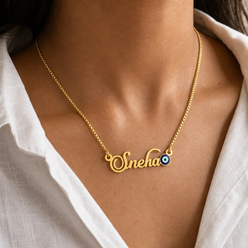 Blue Evil Eye Name Necklace - Worn View Gold-tone name necklace with a blue evil eye accent worn with a white blouse