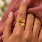 Personalized Butterfly Name Ring worn on a hand against rose-coloured fabric