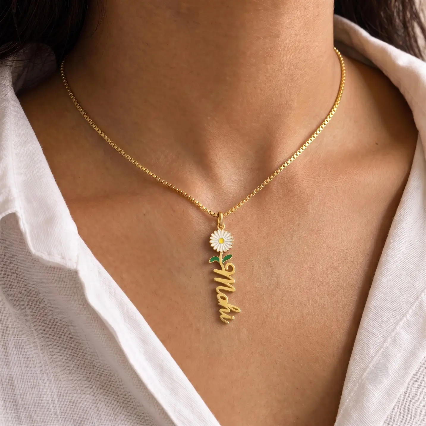 Flower Drop Name Necklace - Worn View Gold-tone vertical name pendant with a daisy flower worn with a white blouse
