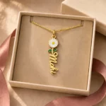 Gold-tone vertical name pendant with a daisy flower displayed in an open beige jewellery box