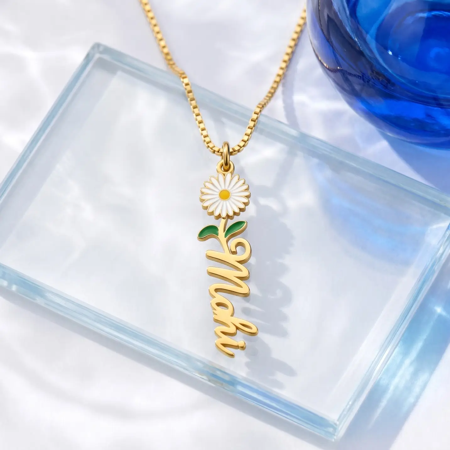 Flower Drop Name Necklace - Glass Display Gold-tone vertical name pendant with a daisy flower on a clear glass display
