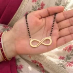 Gold-tone classic infinity pendant on a black-bead chain held in a hand