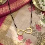 Gold-tone classic infinity pendant on a black-bead chain on floral fabric