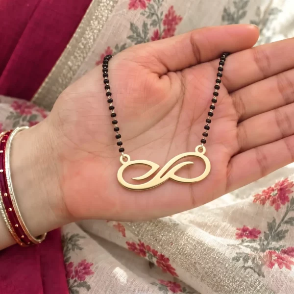 Gold-tone curved infinity pendant on a black-bead chain held in a hand