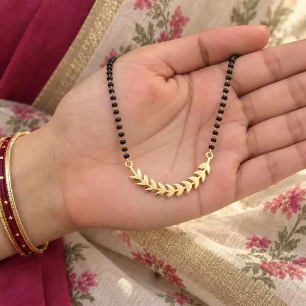 Gold-tone curved leaf pendant on a black-bead chain held in a hand