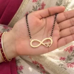 Gold-tone infinity pendant with two open hearts on a black-bead chain held in a hand