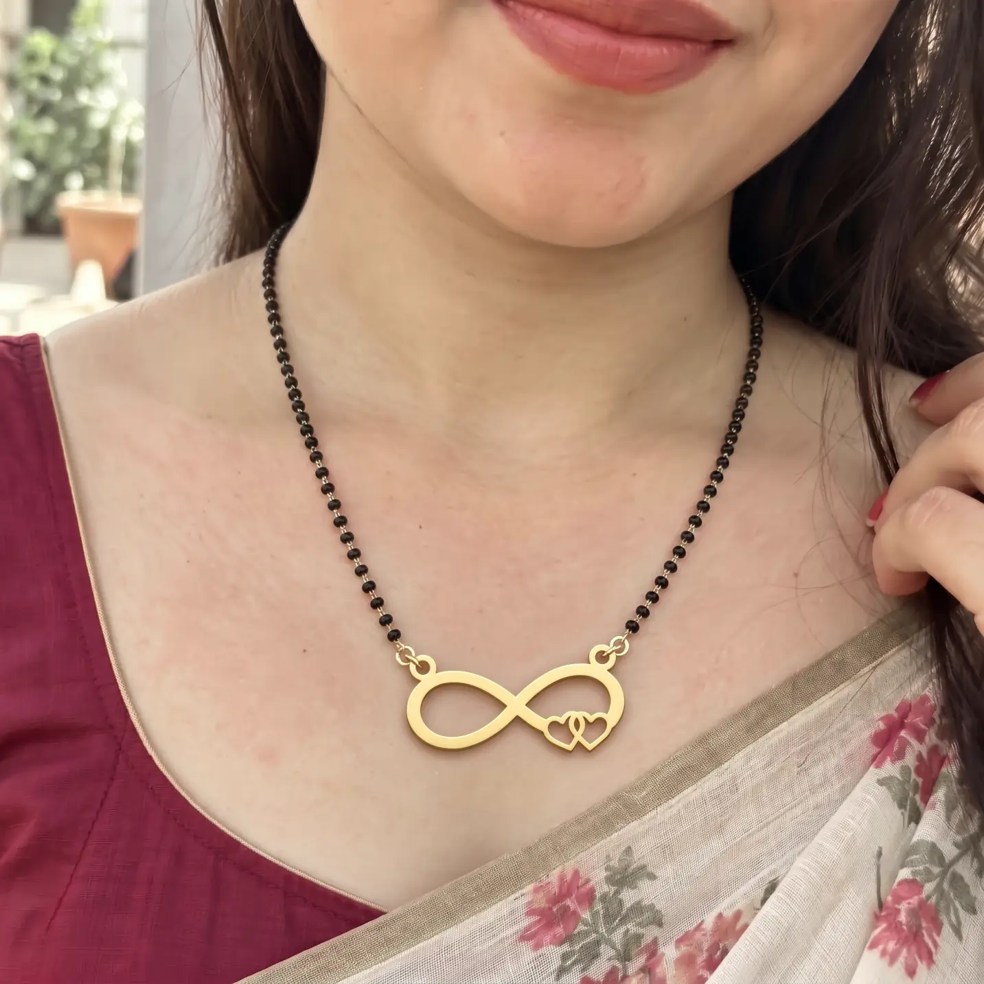 Double Heart Infinity Couple Necklace - Sari Worn View Gold-tone infinity pendant with two open hearts on a black-bead chain worn with a floral sari
