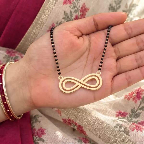 Gold-tone double outline infinity pendant on a black-bead chain held in a hand