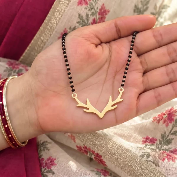 Gold-tone deer antler pendant on a black-bead chain held in a hand