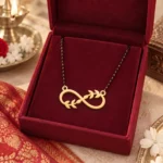 Gold-tone infinity pendant with leaf accents on a black-bead chain displayed in a red jewellery box