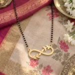 Gold-tone infinity pendant with leaf accents on a black-bead chain on floral fabric