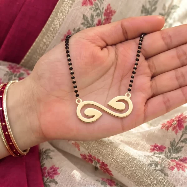 Gold-tone open infinity pendant with curled ends on a black-bead chain held in a hand