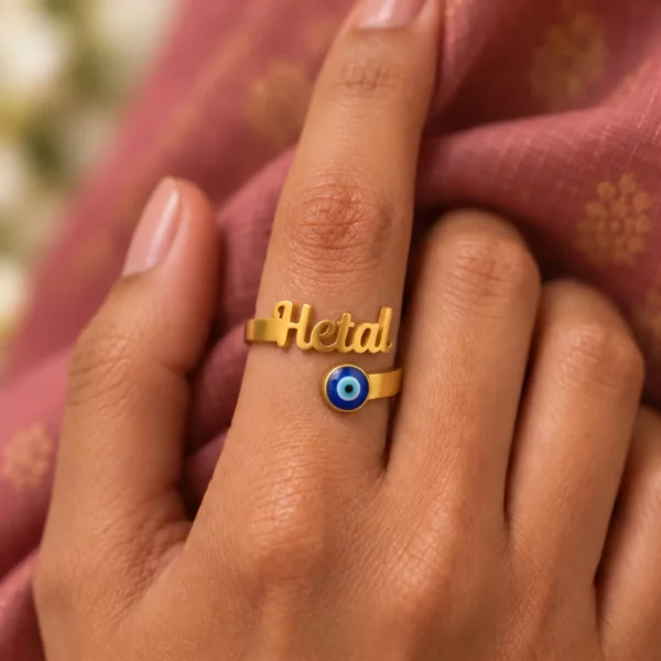 Personalized Blue Evil Eye Name Ring worn on a hand against rose-coloured fabric