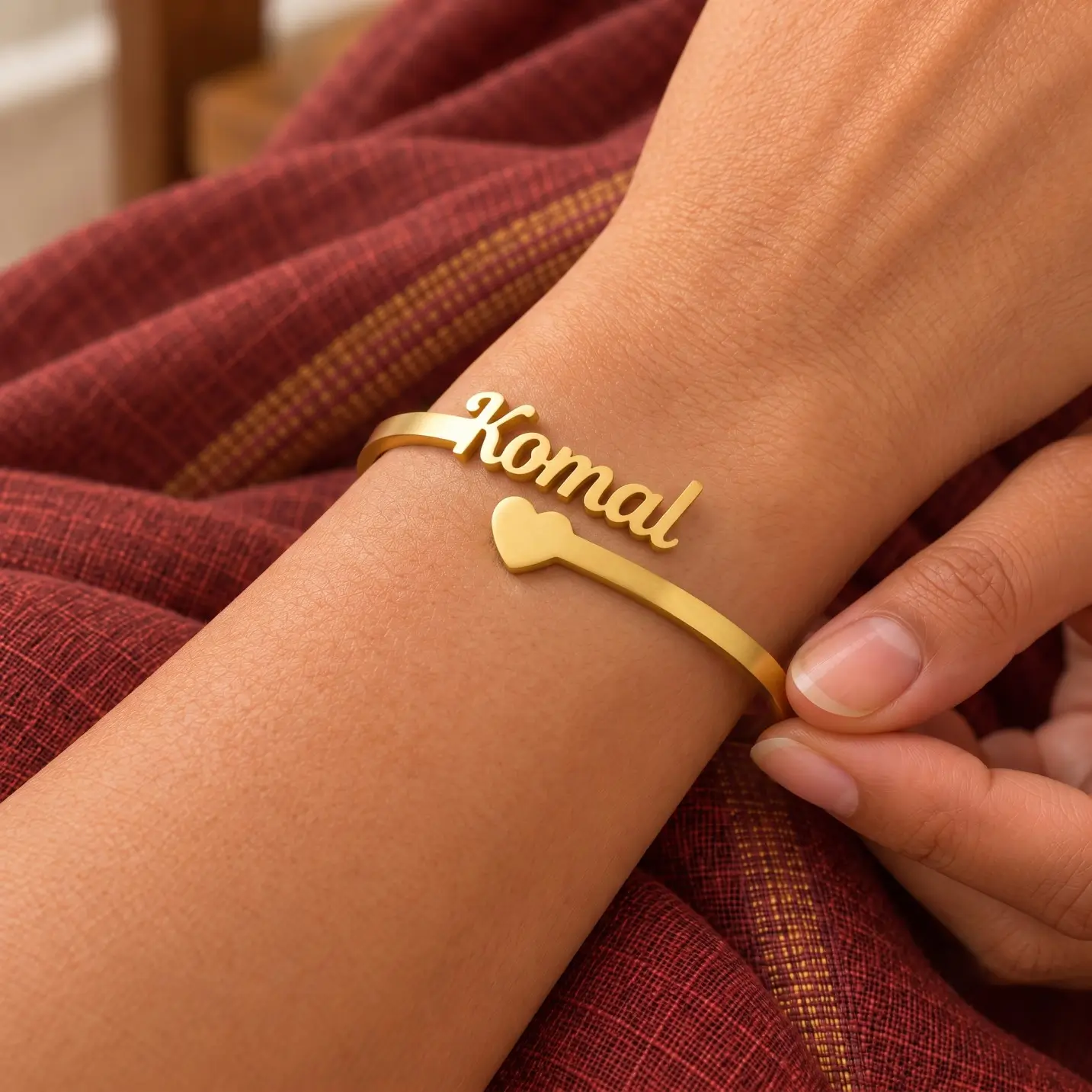 Personalized Heart Name Bracelet - Worn Close-up Personalized Heart Name Bracelet in a golden finish, worn on a wrist beside maroon fabric