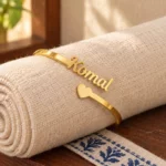 Personalized Heart Name Bracelet in a golden finish, displayed on rolled cream fabric