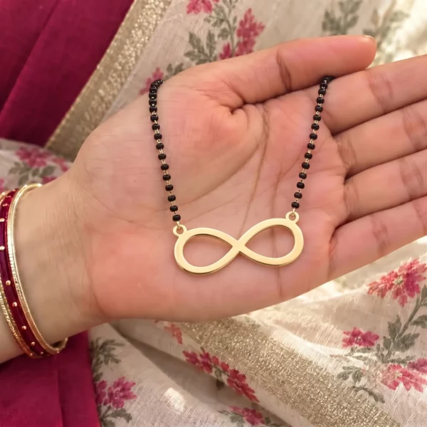 Gold-tone simple infinity pendant on a black-bead chain held in a hand