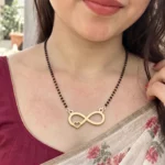 Gold-tone infinity pendant with a small side heart on a black-bead chain worn with a floral sari