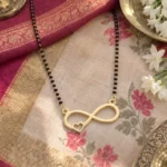 Gold-tone infinity pendant with a small side heart on a black-bead chain on floral fabric