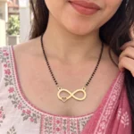 Gold-tone infinity pendant with a small side heart on a black-bead chain worn with a pink and white outfit
