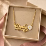 Gold-tone daisy and leaf name necklace displayed in an open beige jewellery box