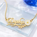 Gold-tone daisy and leaf name necklace on a clear glass display