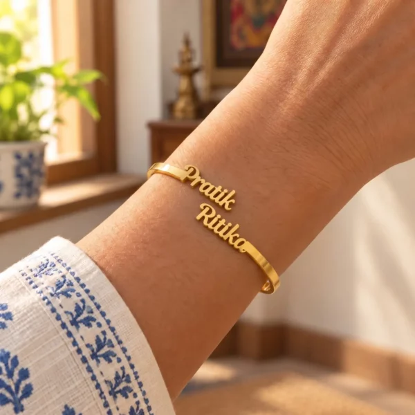Gold-tone personalized couple name bracelet worn on a wrist beside a blue and white sleeve