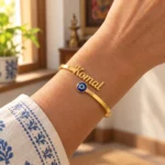 Personalized Evil Eye Name Bracelet in a golden finish, worn on a wrist beside a blue and white sleeve