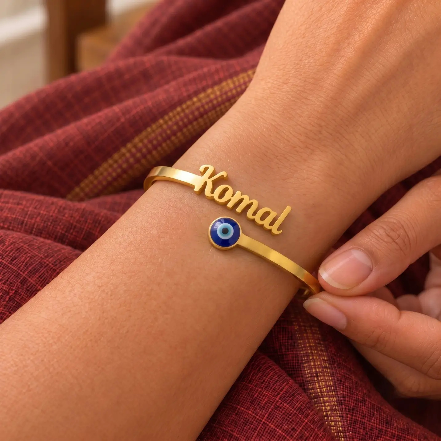 Personalized Evil Eye Name Bracelet - Worn Close-up Personalized Evil Eye Name Bracelet in a golden finish, worn on a wrist beside maroon fabric