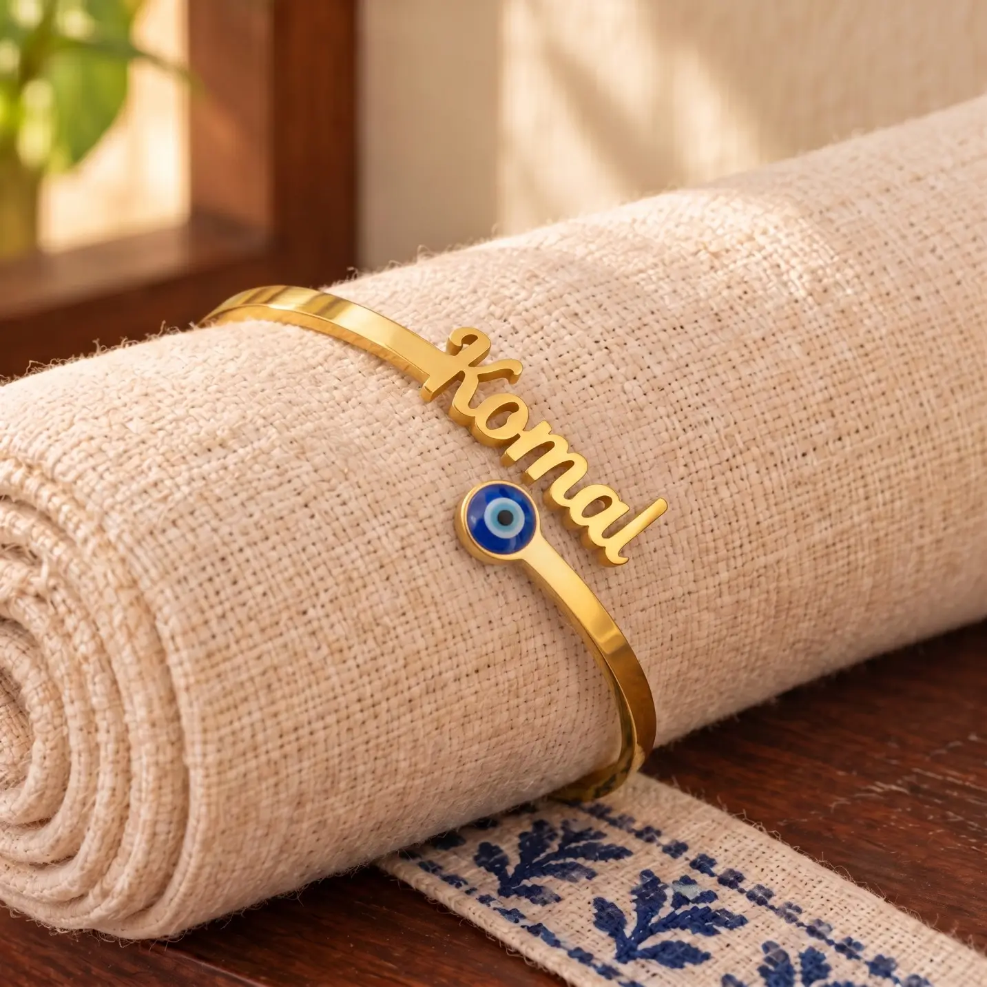 Personalized Evil Eye Name Bracelet - Rolled Fabric Display Personalized Evil Eye Name Bracelet in a golden finish, displayed on rolled cream fabric
