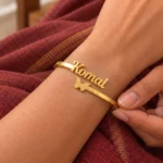 Personalized Butterfly Name Bracelet in a golden finish, worn on a wrist beside maroon fabric