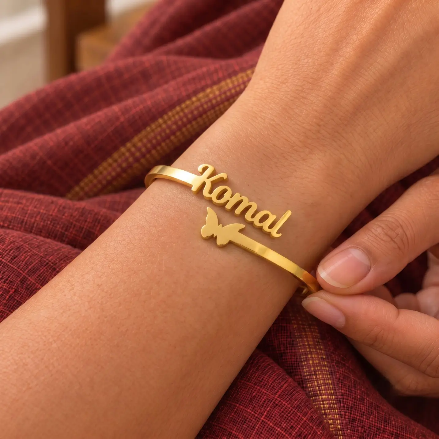 Personalized Butterfly Name Bracelet - Worn Close-up Personalized Butterfly Name Bracelet in a golden finish, worn on a wrist beside maroon fabric