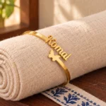Personalized Butterfly Name Bracelet in a golden finish, displayed on rolled cream fabric