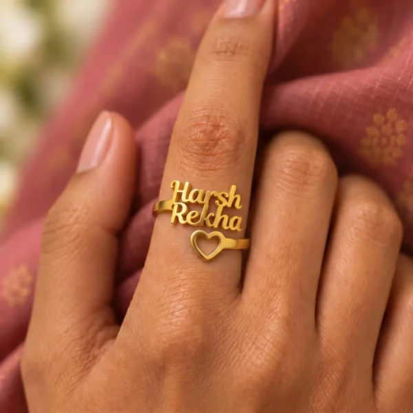 Open Heart Couple Name Ring worn on a hand against rose-coloured fabric