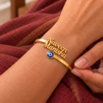 Personalized Evil Eye Couple Bracelet in a golden finish, worn on a wrist beside maroon fabric