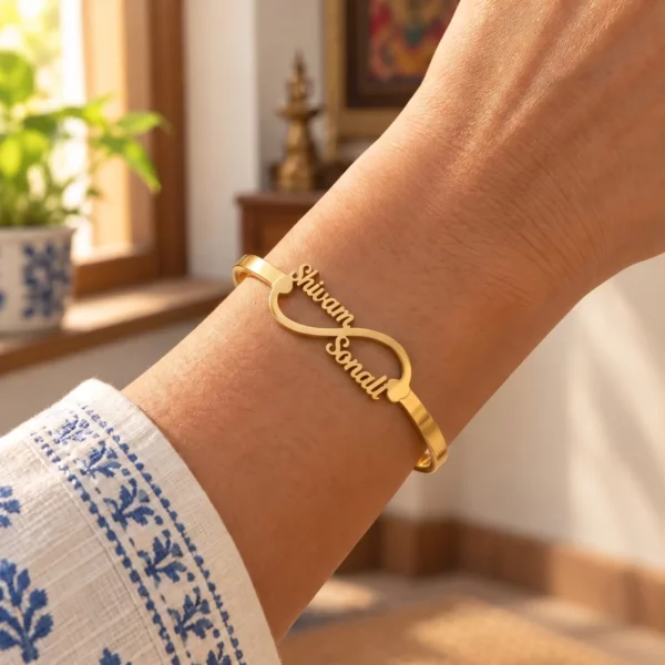 Side Heart Infinity Couple Name Bracelet in a golden finish, worn on a wrist beside a blue and white sleeve